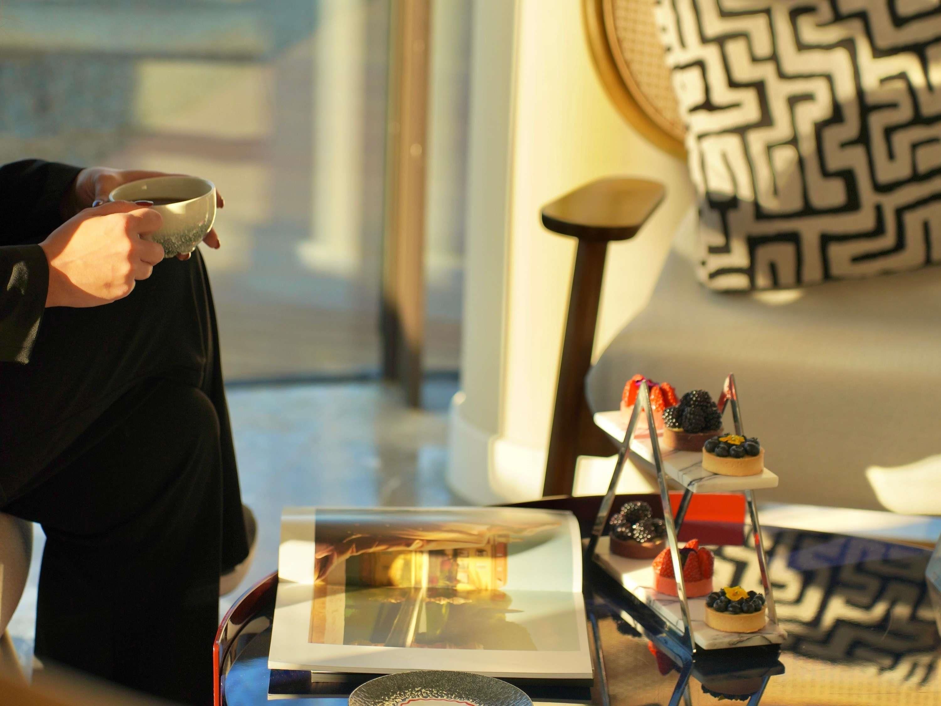 A person holding a cup, a table with desserts, and a patterned wall.