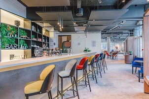 Zona de bar moderna con taburetes altos, una barra con utensilios y estanterías con botellas.