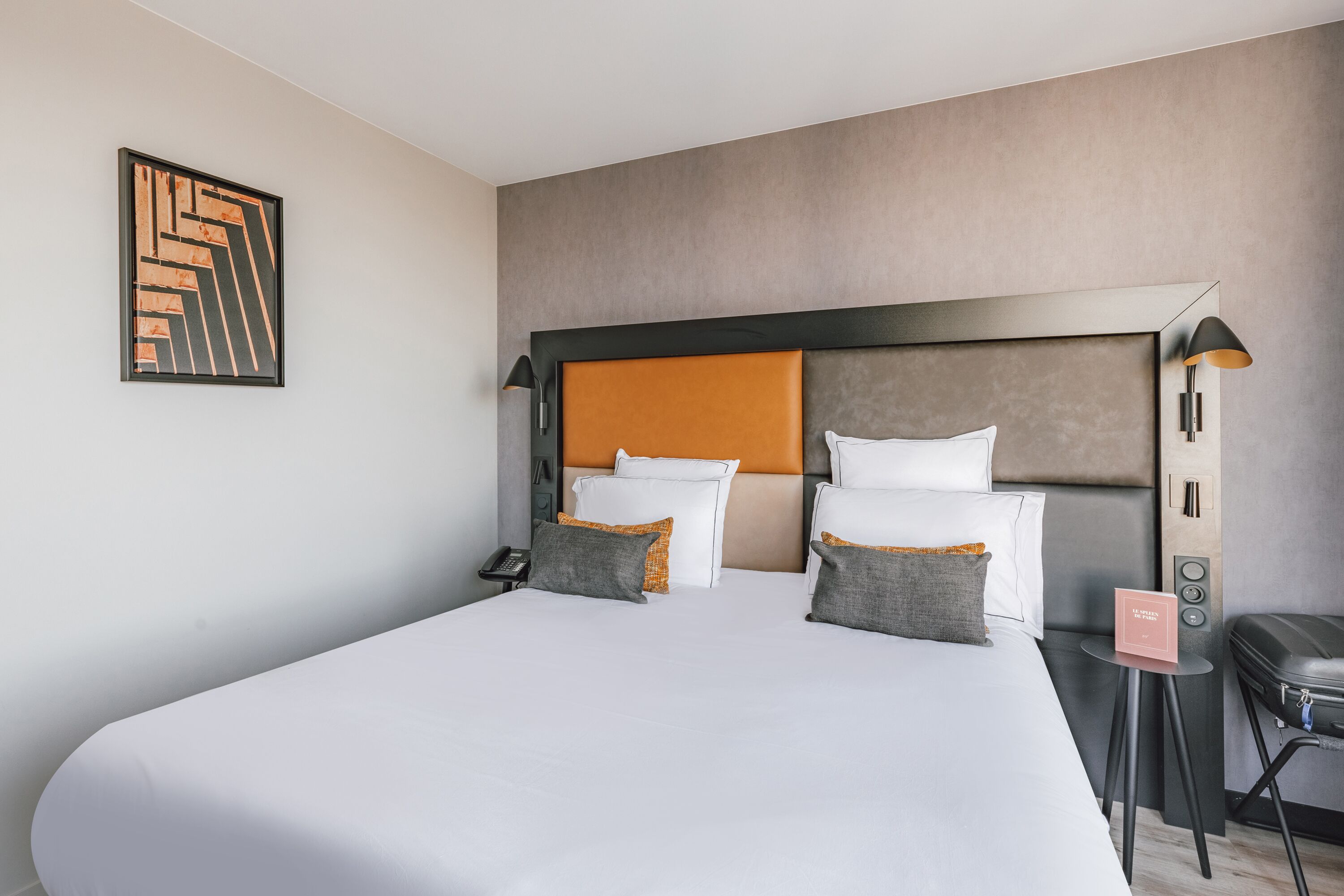 Habitación de hotel con una cama grande, cabecera, mesita de noche, lámpara y una pequeña mesa con un cartel.