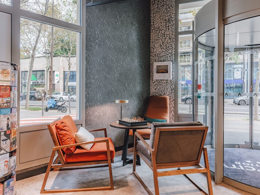 Un interior moderno con dos sillas de madera, una mesita y una estantería llena de revistas.