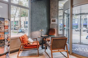 Un interior moderno con dos sillas de madera, una mesita y una estantería llena de revistas.