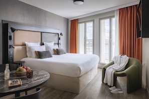 A modern hotel room with a large bed, a round table with breakfast items, a green armchair, and a city view through the windows. - Appart'City Collection Paris Gare de Lyon (Paris)