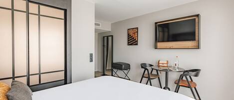 A hotel room with a large bed, a desk with a chair, a small table with a chair, and a TV on the wall.