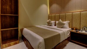 A hotel room with a large bed, wooden wardrobe, and a nightstand with a kettle and remote control. - Hotel Amber Suite (Mumbai)