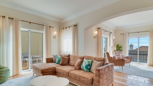 A spacious living area with a large sectional sofa, a round coffee table, and a balcony with a view. - Villa Gasparini (Funchal)