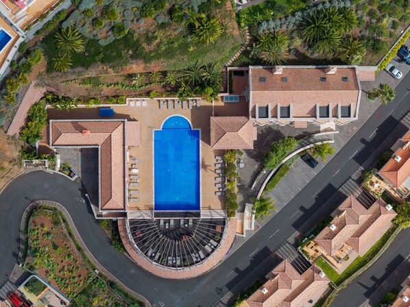 Vista aérea de un resort con piscina central, varias habitaciones para huéspedes y jardines ajardinados.