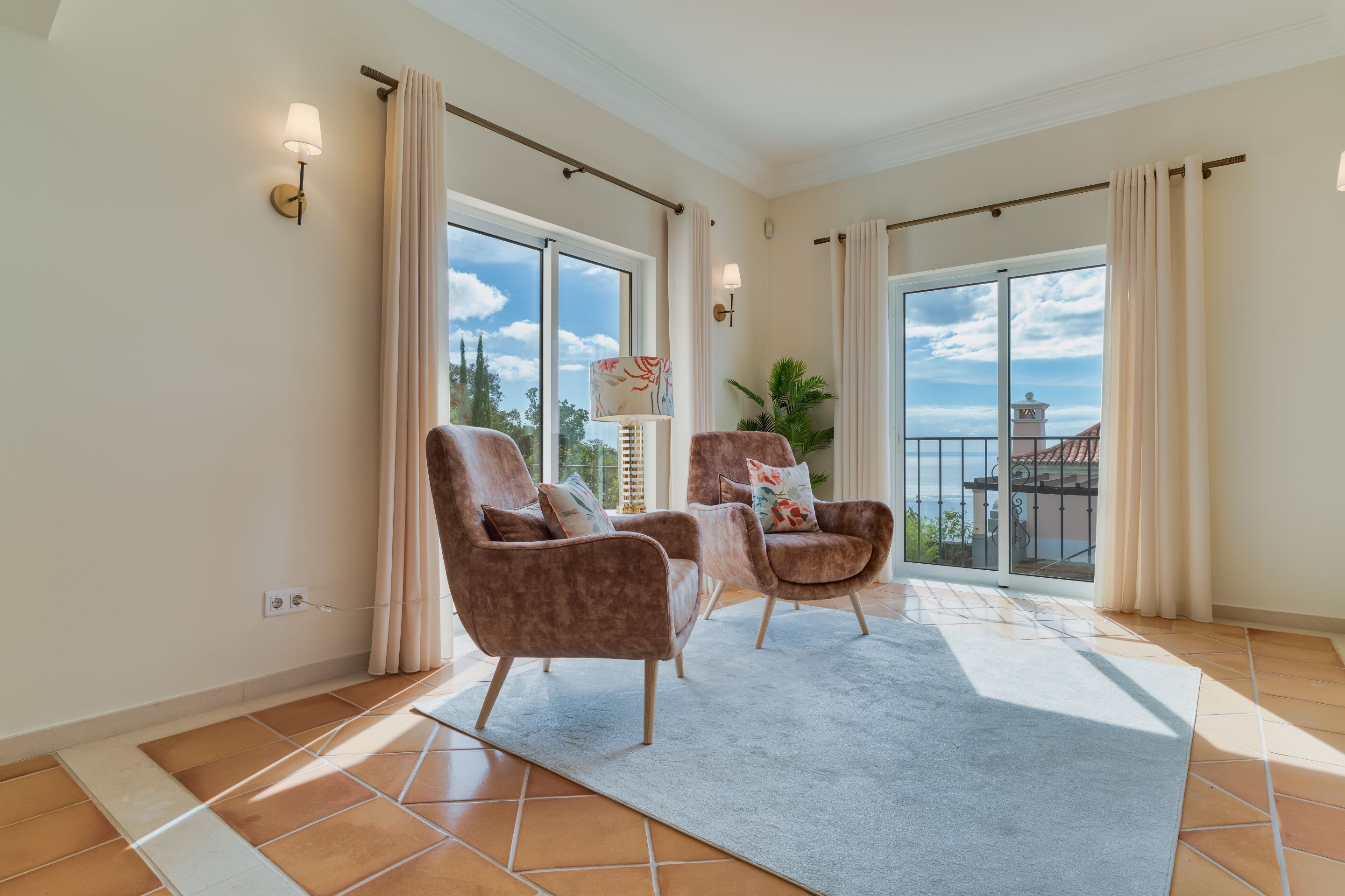 A spacious room with two plush armchairs, a large window with a view of the sea, and a balcony with a railing.