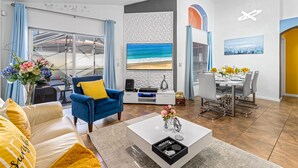 Een moderne woonkamer met een grote televisie, een eethoek en uitzicht op het strand door grote ramen.
