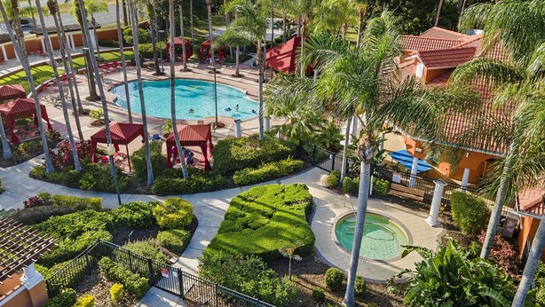 Een resort met een centraal gelegen zwembad, palmbomen en gebouwen met rode daken.