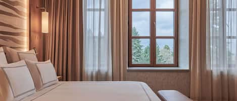 A hotel room with a large bed, a bench, a window with curtains, and a wall with a patterned design.