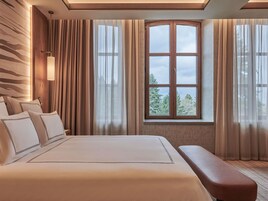 Quarto de hotel com uma cama grande, um banco, uma janela com cortinas e uma parede com design estampado.