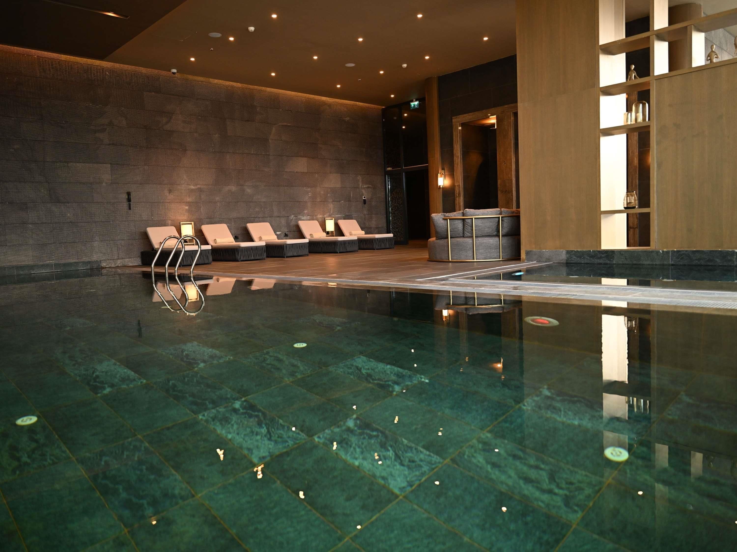 A modern indoor swimming pool with lounge chairs and a wooden reception area.