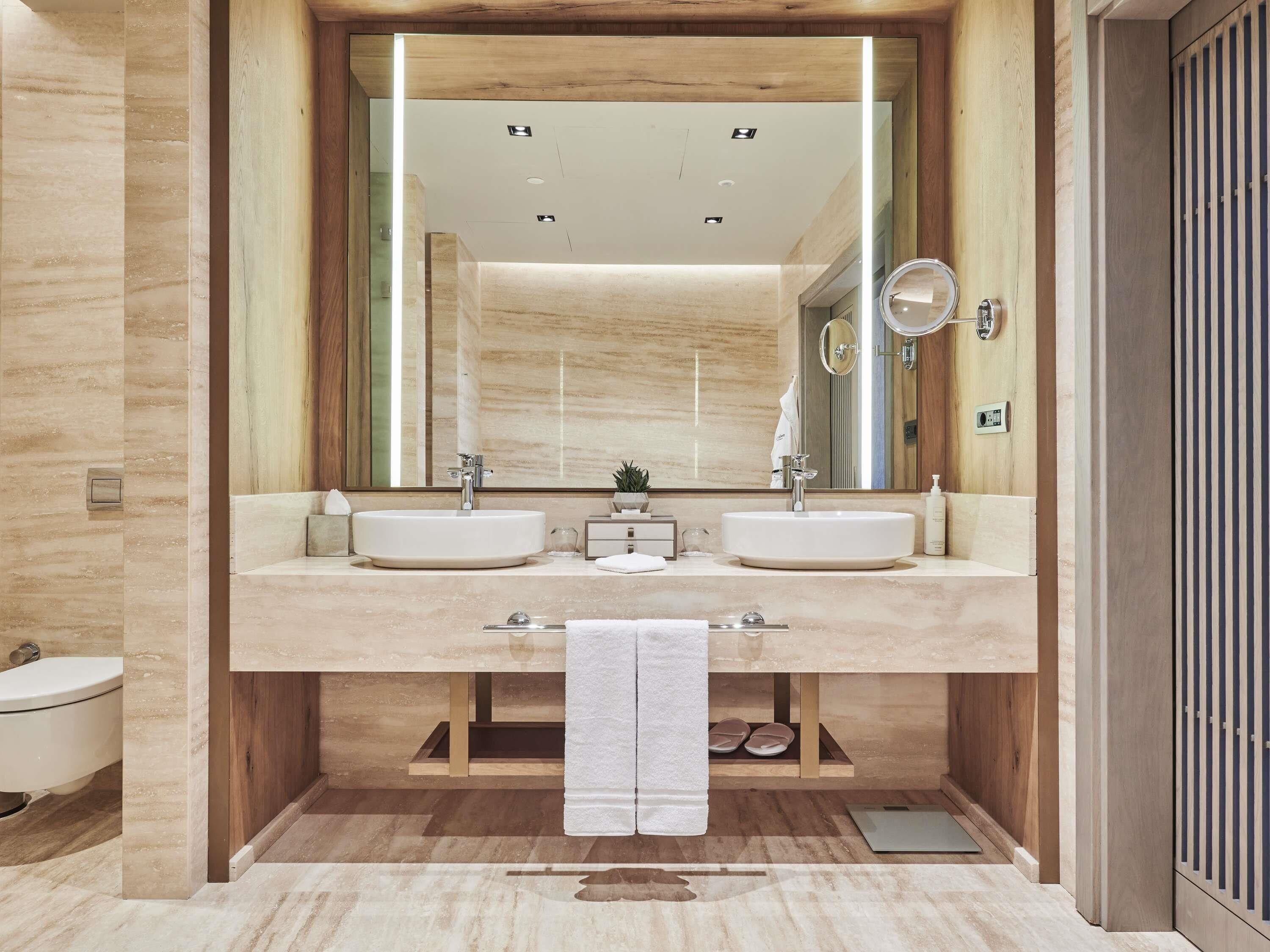 A modern bathroom with two sinks, a large mirror, and a towel rack.