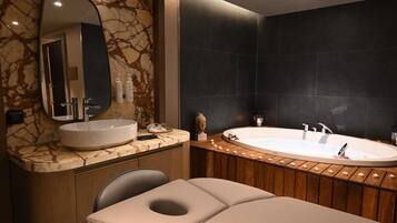 Un baño moderno con tocador de mármol, una bañera amplia y un banco de madera.