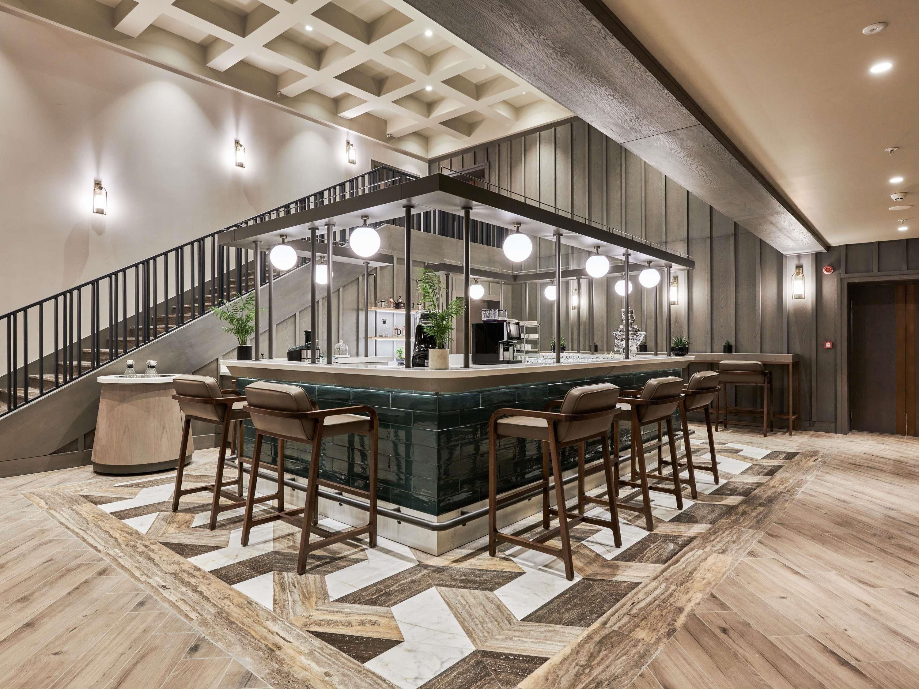 A bar area with a central island, multiple stools, a staircase, and a patterned floor.