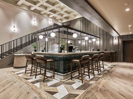 Zona de bar con una isla central, varios taburetes, una escalera y un suelo estampado.