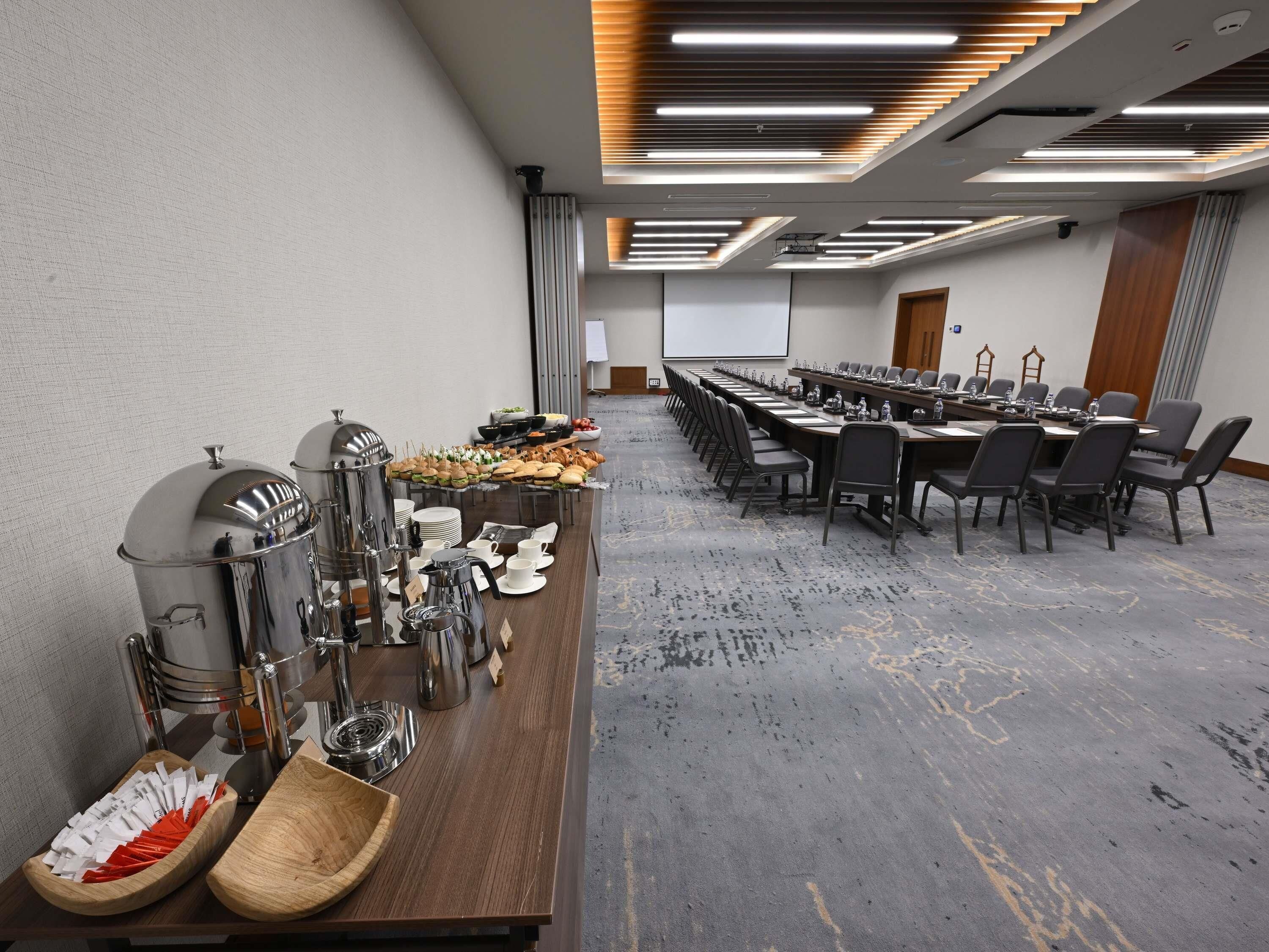 A conference room with a long table, chairs, and a buffet setup with food and beverages.