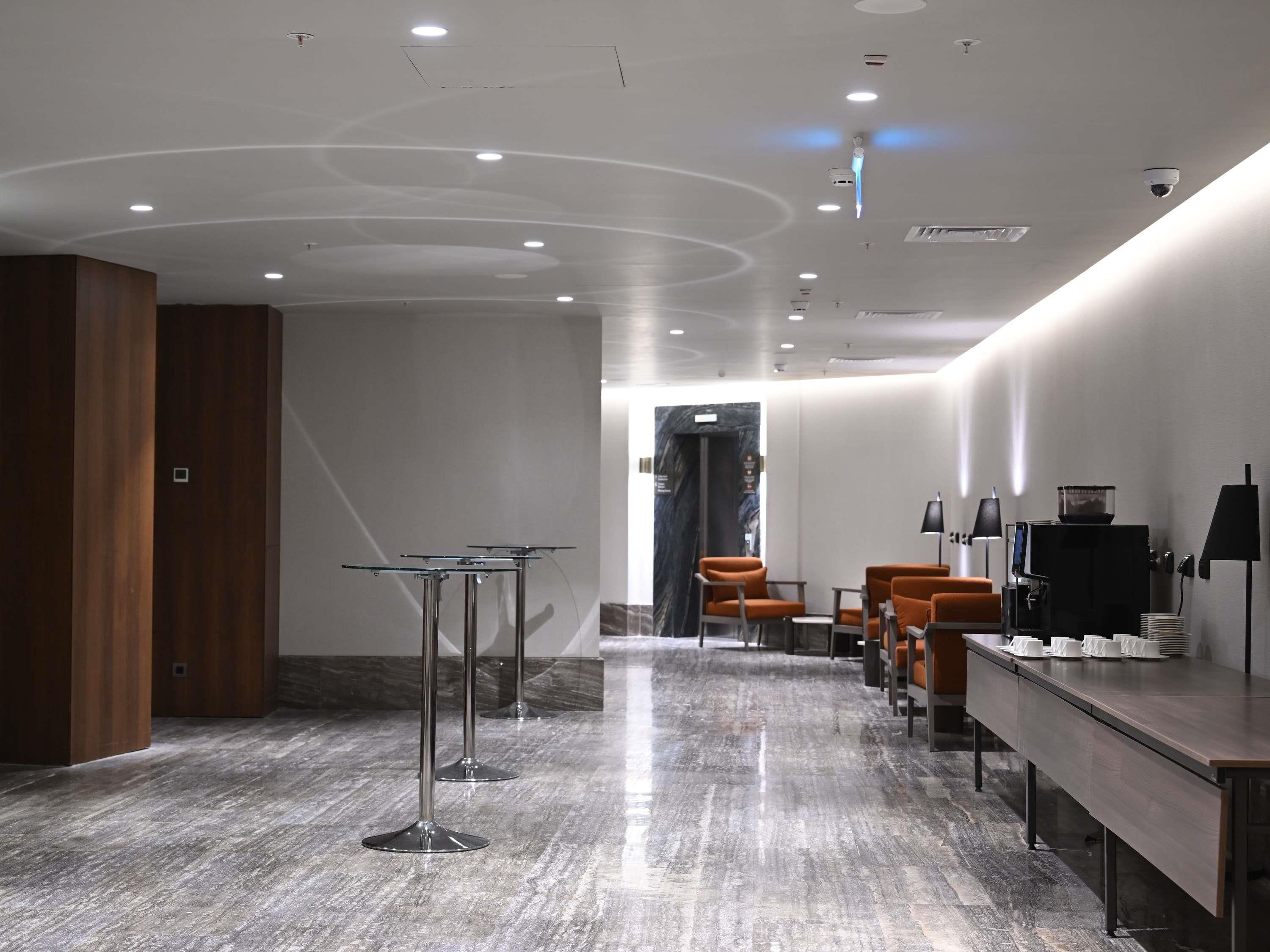 Un hall d’hôtel moderne avec un sol en marbre, un comptoir d’accueil, un espace salon et une table de conférence.