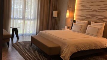 Habitación de hotel con una cama grande, una mesita pequeña y vistas a través de cortinas traslúcidas.