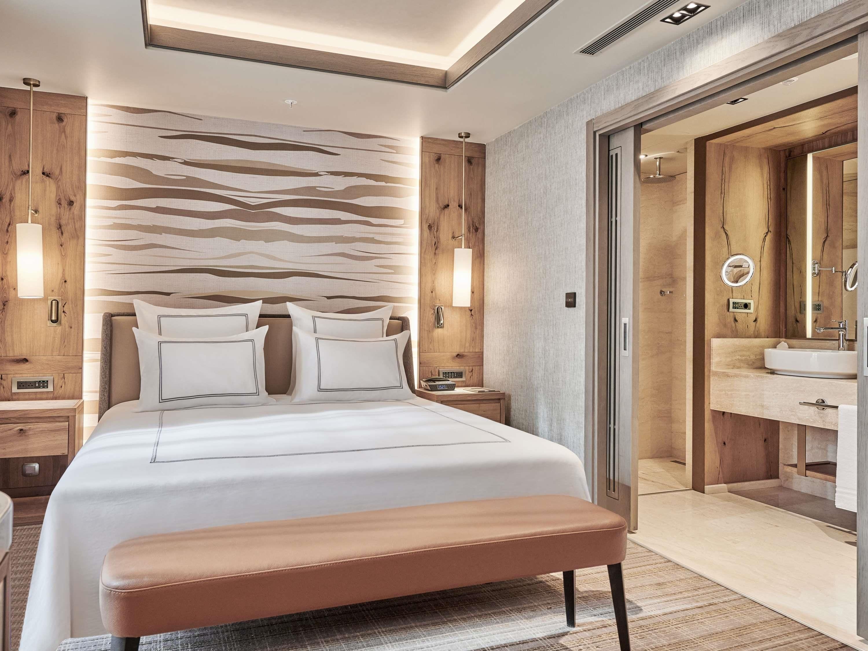 A modern hotel room with a large bed, wooden headboard, and a bathroom with a large mirror and sink.