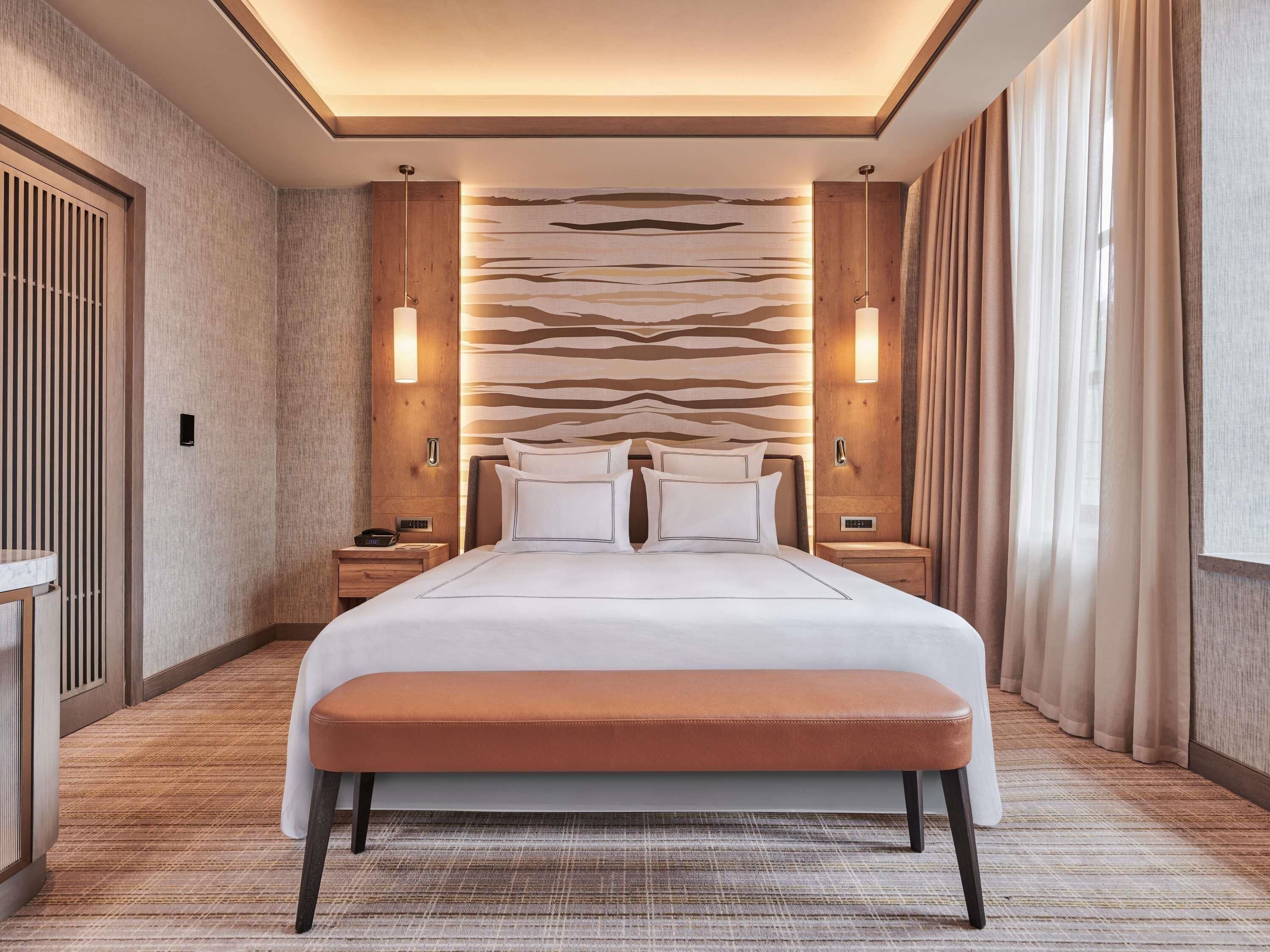 A hotel room with a large bed, bedside tables, a bench, and a patterned wall.