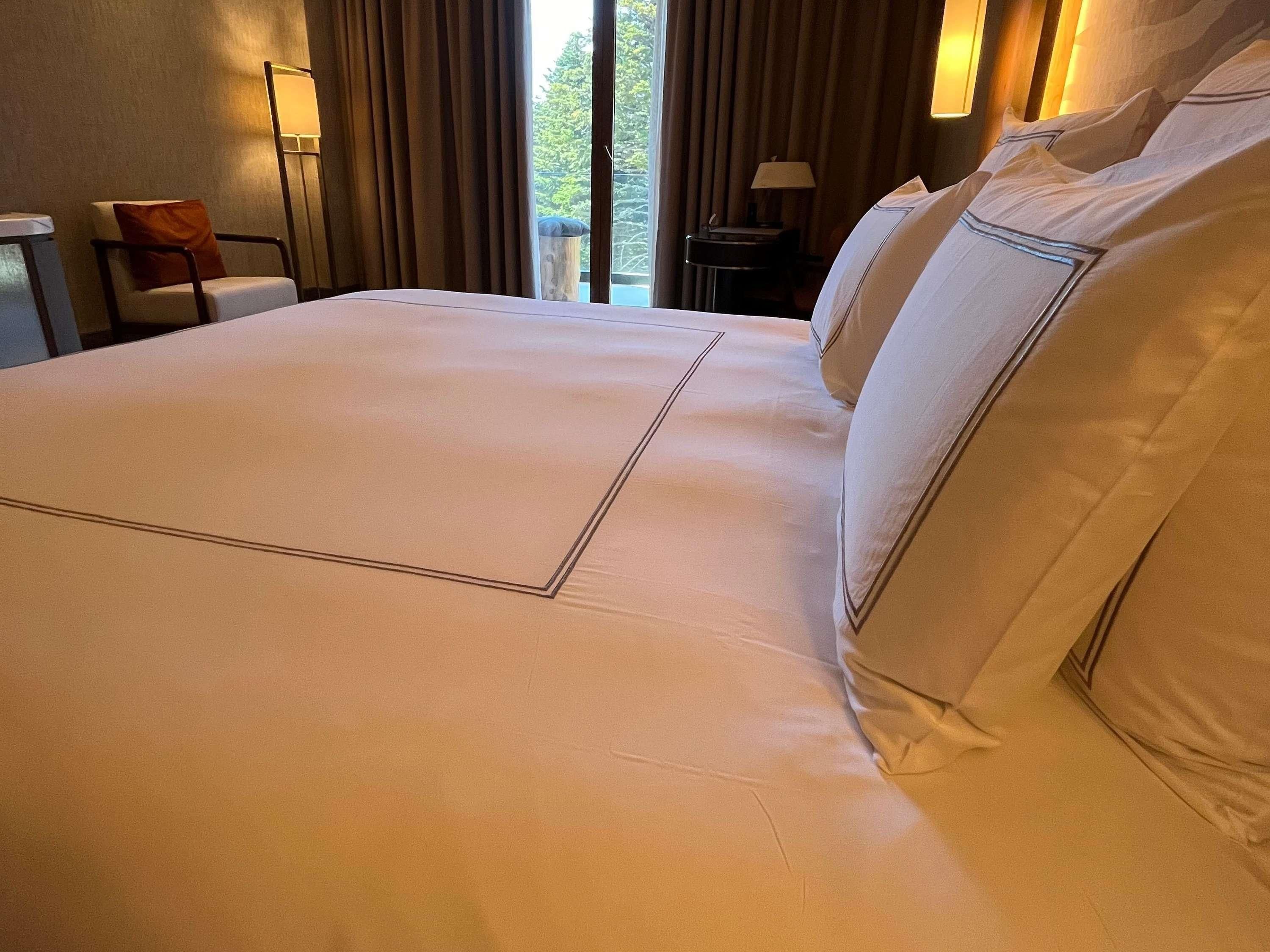 Una cama grande con cabecera, una silla, una mesita y una lámpara.