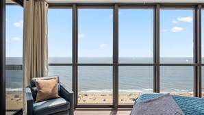 Una habitación con un amplio ventanal que da a una playa, una silla y una cama.