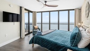 Un dormitorio con una cama grande, ventilador de techo, televisión y vista al océano.