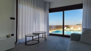 A modern living room with a sofa, a small round table, and a view of a swimming pool through large sliding glass doors. - Villa with sea view (Finestrat)