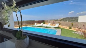 A view from a window to a backyard with a swimming pool, a potted orchid, and a stone wall. - Villa with sea view (Finestrat)