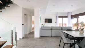 A modern living room with a grey sofa, a dining table with chairs, and a staircase with glass railings. - Villa with sea view (Finestrat)