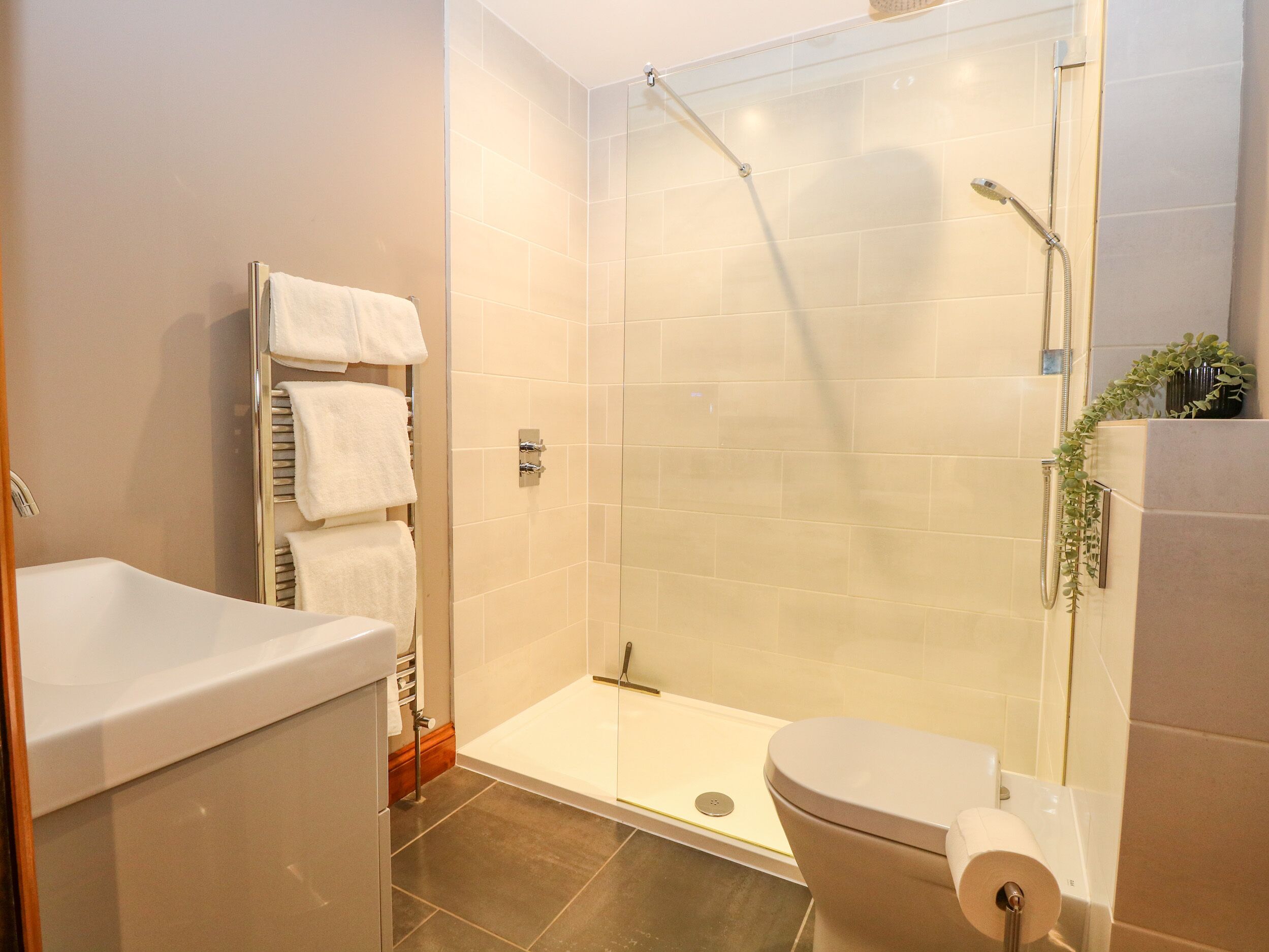 Een moderne badkamer met een douche met glazen wand, een wit toilet en een wastafel met een handdoekrek.