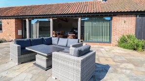 A patio area with wicker furniture, a brick building, and a tiled roof. - Shorthorn Barn (Norwich)