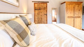 A bedroom with a bed, wooden wardrobe, and a painting on the wall. - Shorthorn Barn (Norwich)