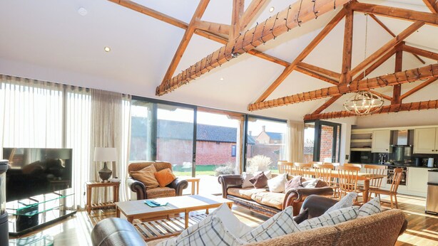 A spacious living room with a large sofa, a television, and a dining area with wooden furniture. - Shorthorn Barn (Norwich)