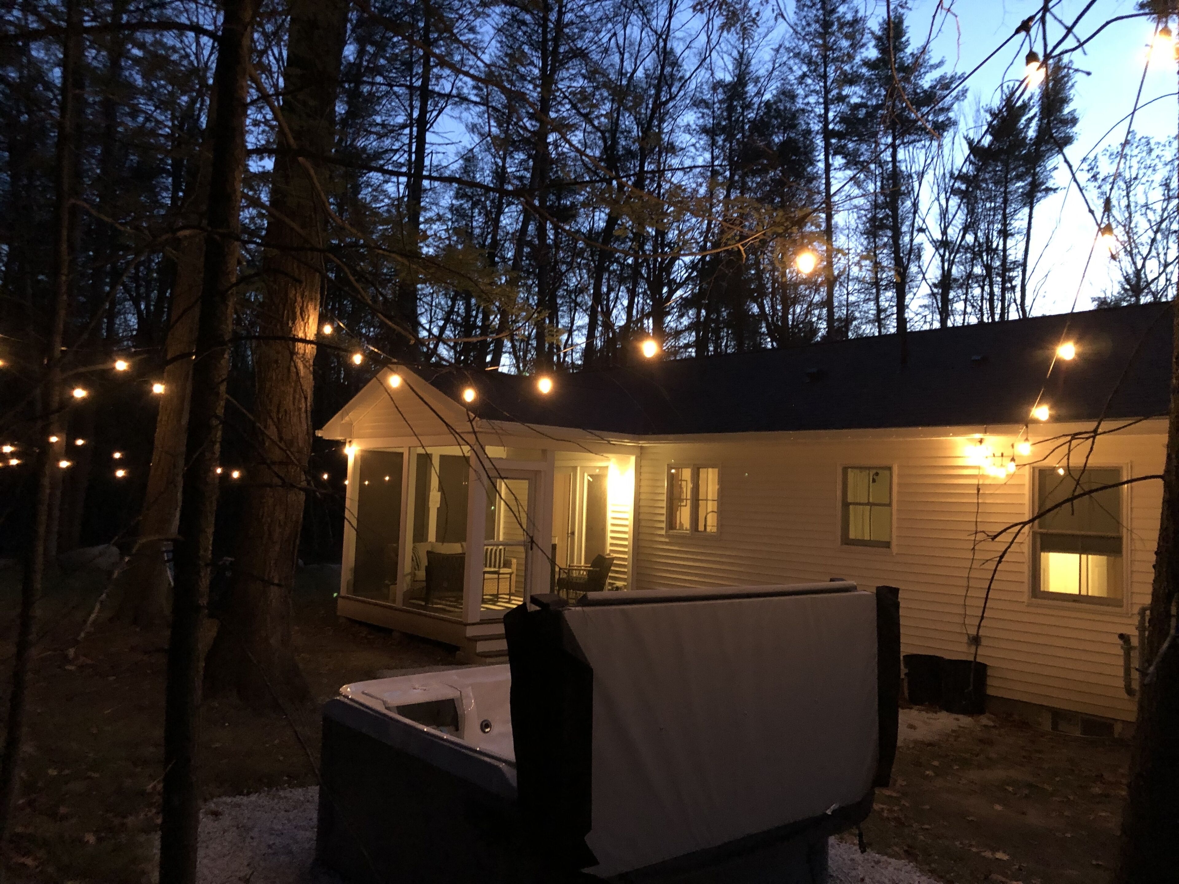A cabin with a covered outdoor seating area, surrounded by trees and string lights.