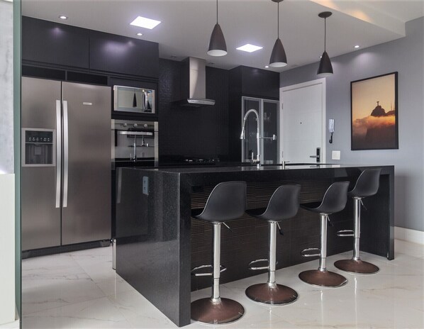Una cocina moderna con una isla central, electrodomésticos de acero inoxidable y taburetes de bar.