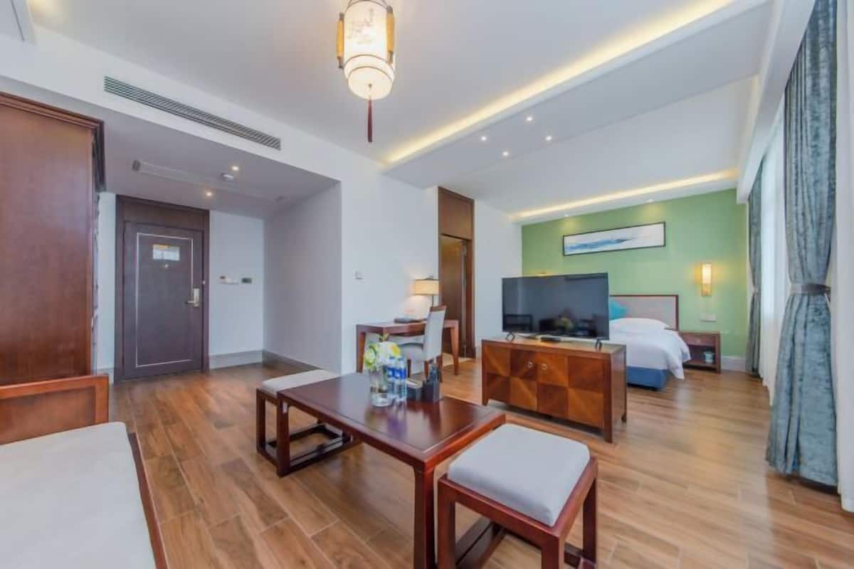 Una habitación de hotel con piso de madera, televisión, cama, escritorio y una silla.