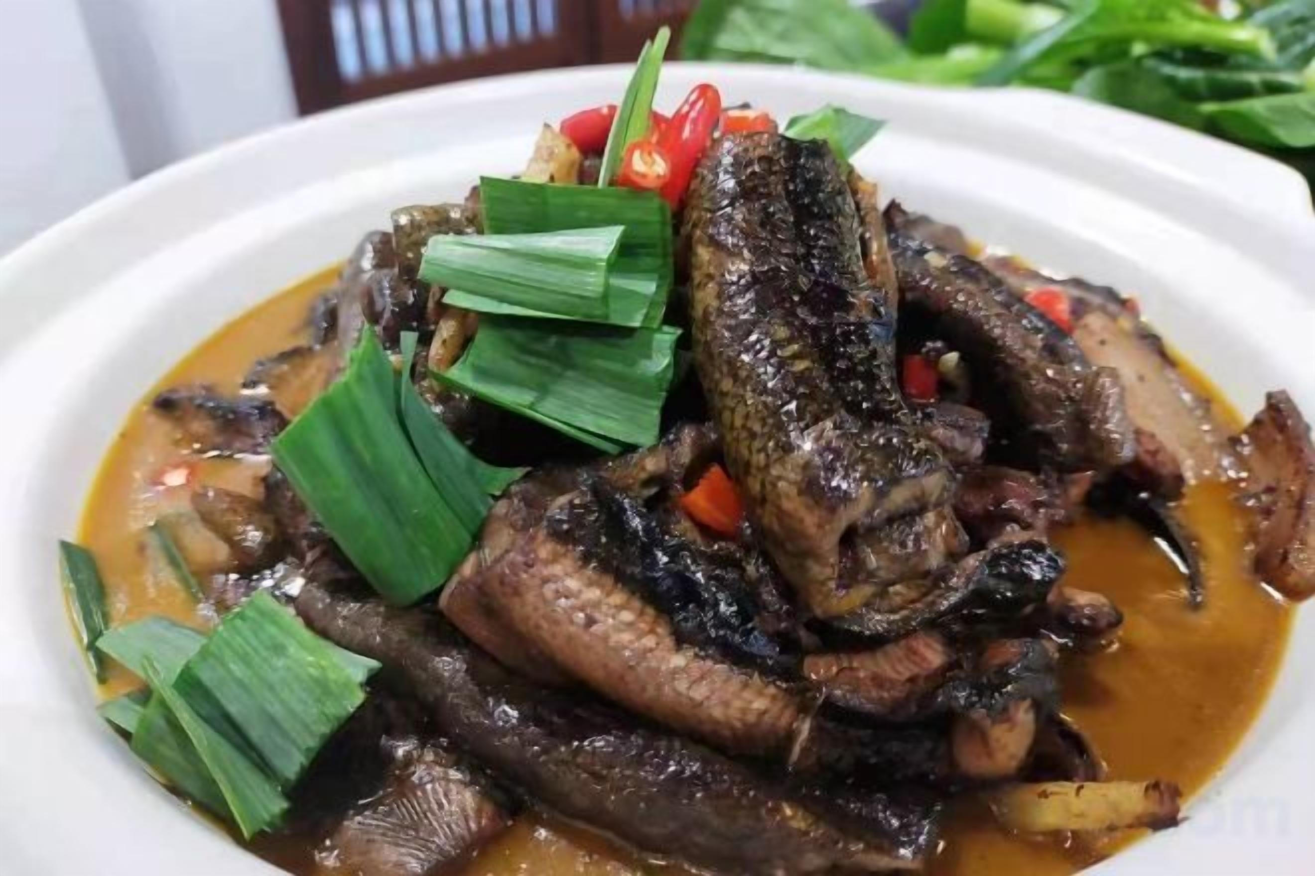 A dish with grilled meat and vegetables in a sauce, garnished with green leaves and red chili.
