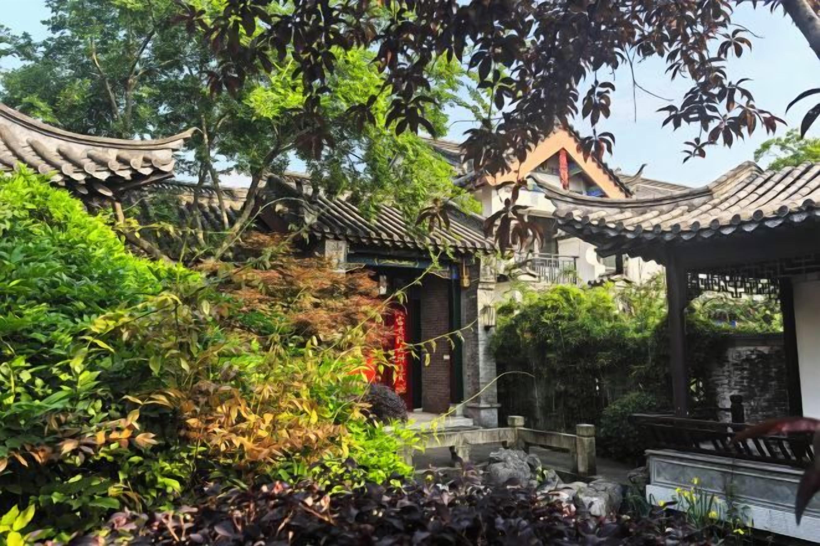 A traditional Chinese garden with a pavilion, stone bridge, and lush vegetation.
