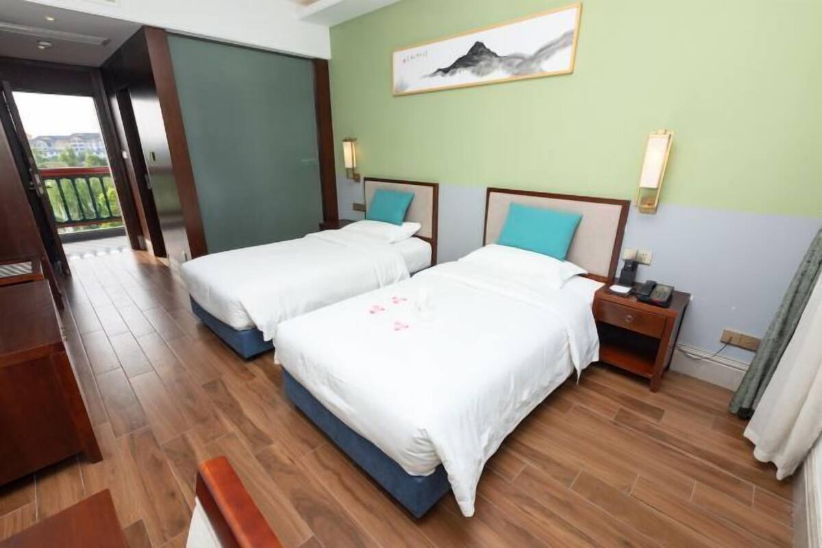 Habitación de hotel con dos camas, piso de madera, un cuadro en la pared y vistas a través de una puerta abierta.