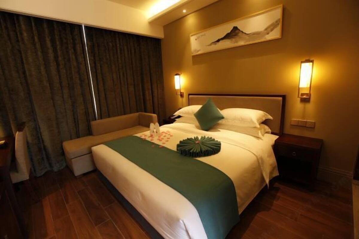 Una habitación de hotel con cama, mesitas de noche, un sofá y un cuadro en la pared.