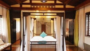 Ein traditionell eingerichteter Raum mit einem Bett unter einem Baldachin, Holzdielen und einer Decke mit freiliegenden Balken.