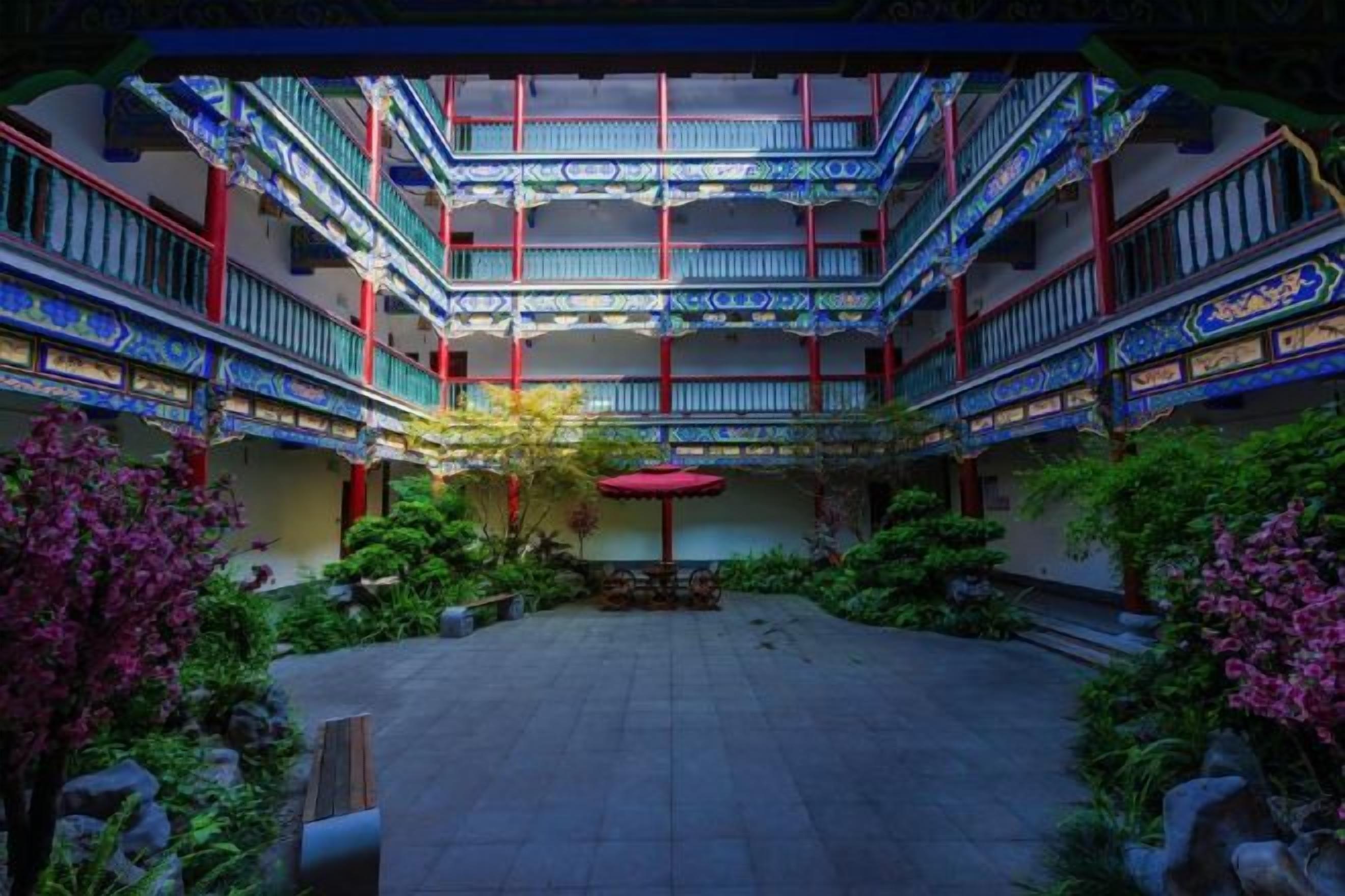 Une cour traditionnelle dotée de plusieurs niveaux de balcons, entourée d’une végétation luxuriante et comprenant un espace de repos central.