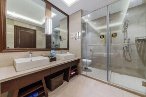 A modern bathroom with a large mirror, two sinks, a shower, and a toilet.