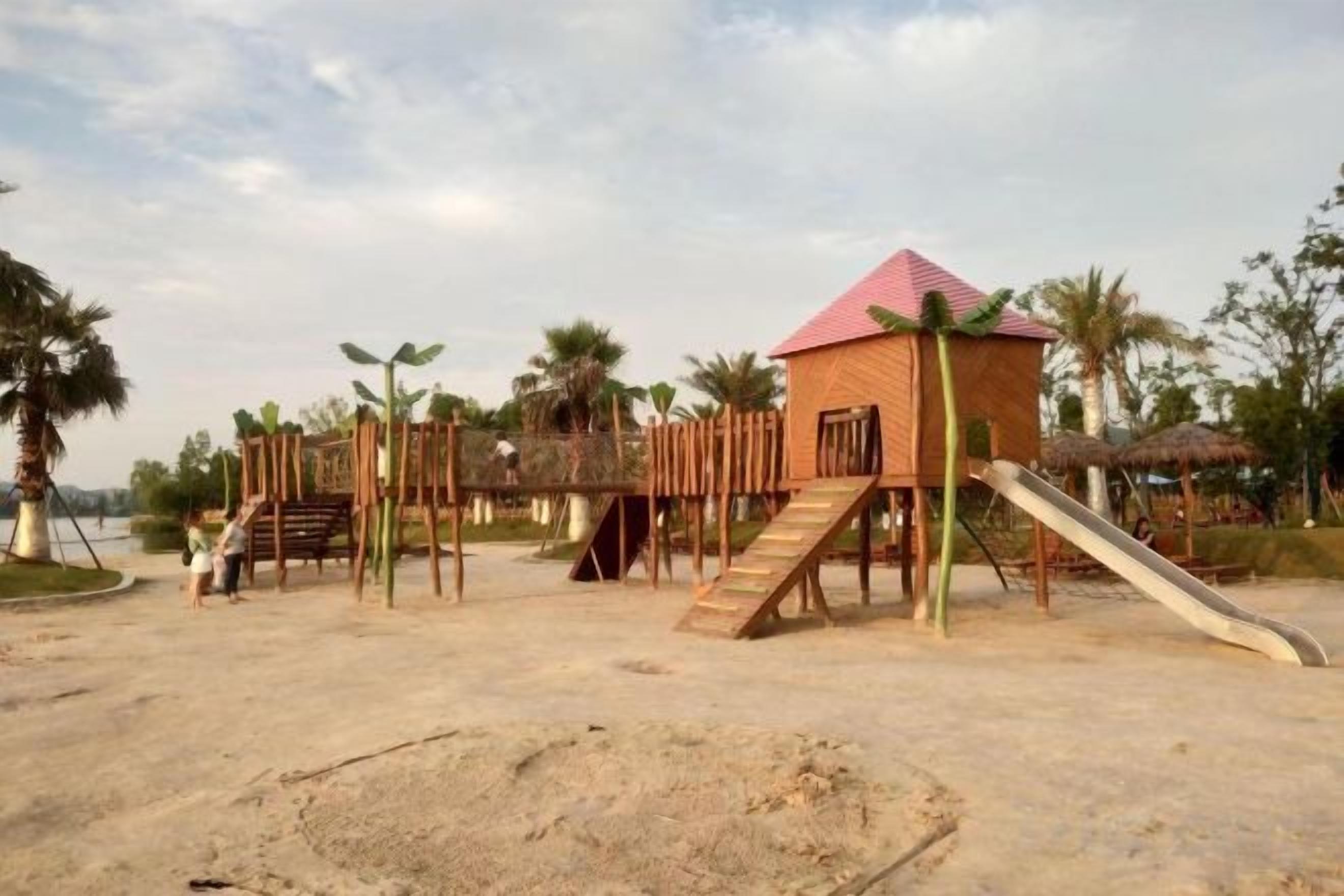 A playground with a slide, climbing structures, and a small building with a red roof.