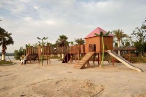 A playground with a slide, climbing structures, and a small building with a red roof.