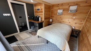 A compact room with a bed, a small desk with a coffee machine, and a wooden wall with a picture.