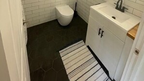 A bathroom with white subway tiles, a white toilet, a sink with a mirror, and a dark floor.