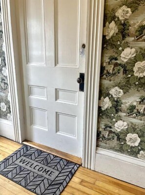Traditional door with a welcoming doormat and floral wallpaper.